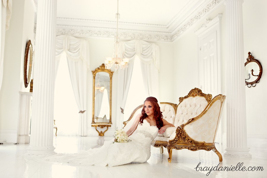 bride sitting on floor leaning against gold and white couch in all white room by Bray Danielle Photo